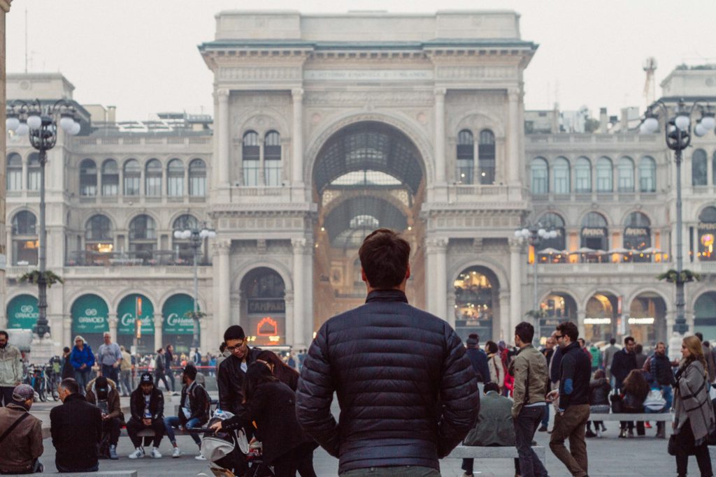 Featured in Best Destinations for Solo Travelers by Jaya Travel & Tours, this image shows the back of a young man looking at an architectural monument in Italy with a crowd.