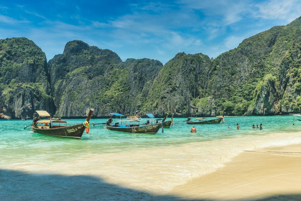 Featured in "Which Country Should You Visit Quiz" by Jaya Travel & Tours, this image shows a beach in Thailand with boats and beautiful blue water.