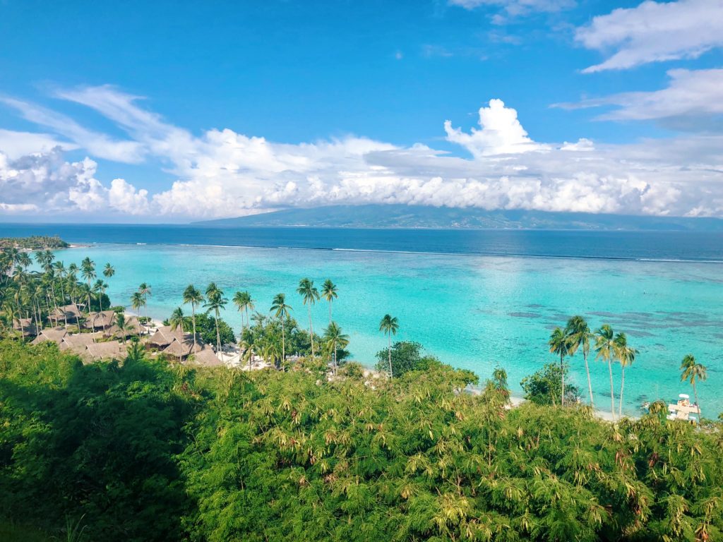Featured in Winter Travel Destinations by Jaya Travel & Tours, this image shows a tropical island in French Polynesia with bright blue water and lush trees.