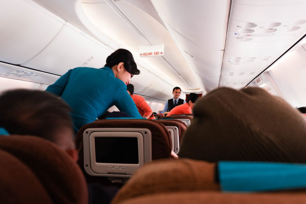 Featured in Guide to Flight Classes by Jaya Travel & Tours, this image shows the economy airline cabin with a flight attendant.