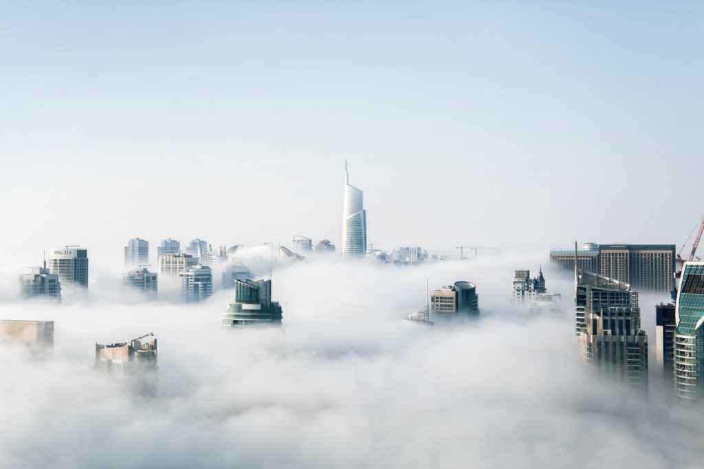 Featured in Futuristic Cities for Vacation by Jaya Travel & Tours, this image shows a cityscape of skyscrapers with clouds blocking some of the view.