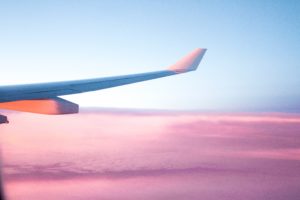 Featured in Guide to Flight Classes by Jaya Travel & Tours, this image shows the wing of an airplane flying with a pink sunset.