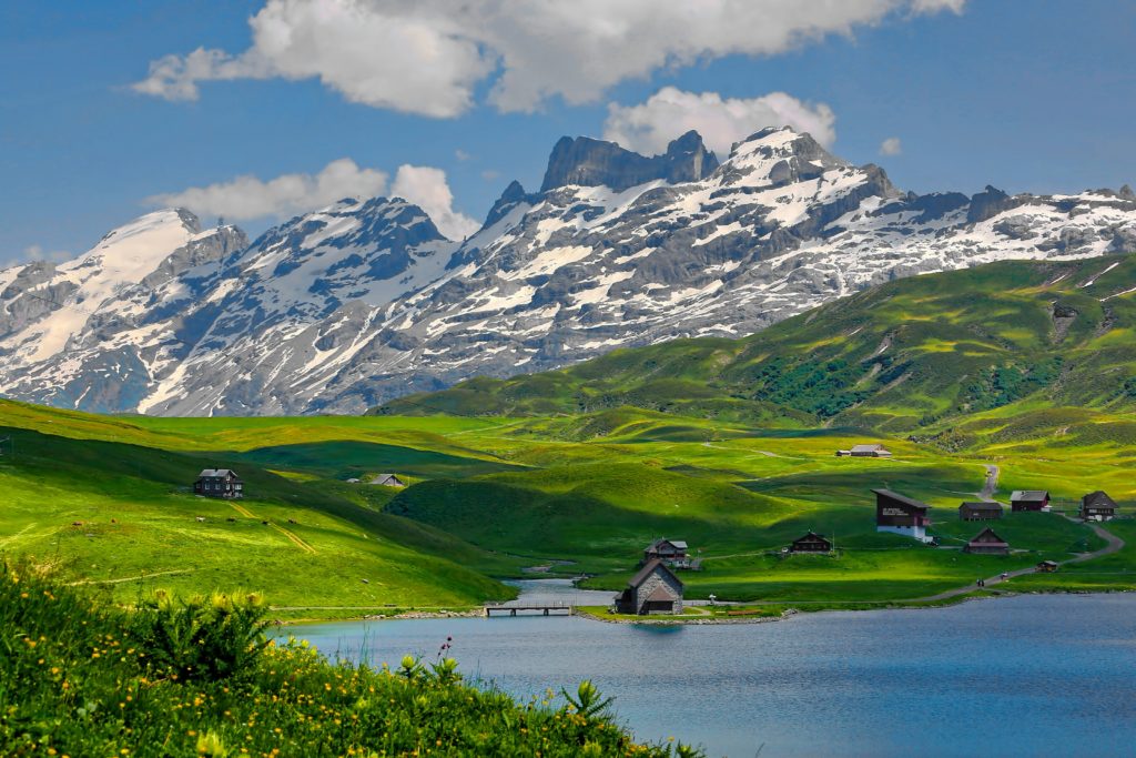 Featured in the Jaya Travel & Tours blog, "Jaya's Best of Europe Tour," this image shows the stunning Swiss alps and a green field behind a lake.