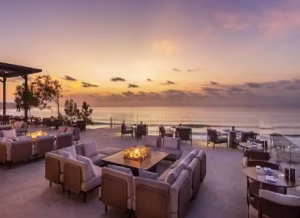 Akasa Jumeirah - Jaya Travel & Tours Beachfront outdoor lounge at sunset with fire pit seating and tables facing the ocean.