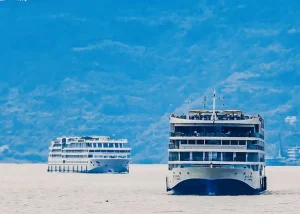 Chongqing - Jaya Travel & Tours Two white passenger ferries glide on calm water with a hazy mountain range in the background.