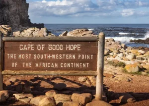 cape-of-good-hope - Jaya Travel & Tours Wooden sign reading 'Cape of Good Hope, the most south-western point of the African continent,' on a rocky coastal foreground with the ocean beyond.