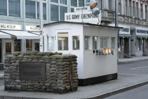 checkpoint-charlie - Jaya Travel & Tours White security booth labeled 'US Army Checkpoint' with sandbag barricade on a city street.