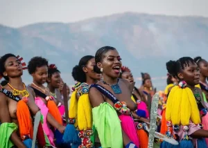 eSwatini - Jaya Travel & Tours A vibrant group of dancers in colorful costumes and accessories performing together outdoors, with mountains in the background.