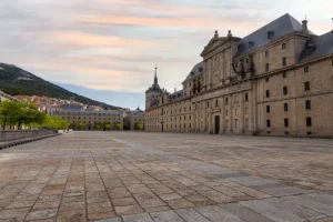 el-escorial - Jaya Travel & Tours Expansive stone plaza in front of a grand historic building with towers and a detailed facade under a pastel sky.
