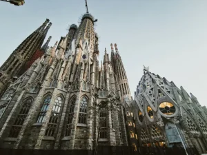 gaudis-la-sagrada - Jaya Travel & Tours Sagrada Família facade with towering spires under a clear sky, showcasing intricate stonework and modernist Gothic design of Barcelona's landmark.