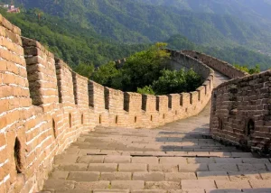great-wall-china - Jaya Travel & Tours Curving stone pathway along the Great Wall with crenellated walls and green mountains in the background