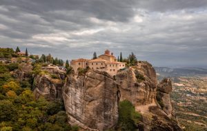 meteora - Jaya Travel & Tours Monastery perched on a tall rock cliff under a cloudy sky.