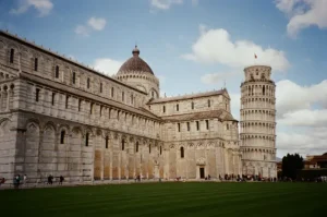 piazza-dei-miracoli - Jaya Travel & Tours Pisa Cathedral and the Leaning Tower of Pisa in the Piazza dei Miracoli, with a well-kept green lawn in the foreground and a blue sky above.