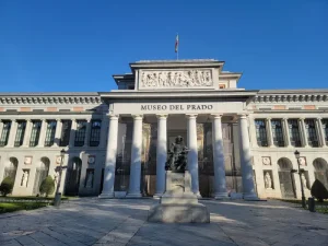prado-museum - Jaya Travel & Tours Front façade of the Museo del Prado with a columned portico and a statue in the plaza in front of the entrance.