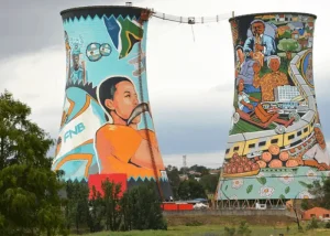 soweto - Jaya Travel & Tours Two tall cooling towers painted with vibrant murals depicting people and scenes, connected by a skybridge.