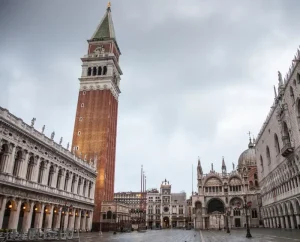 st-marks-square - Jaya Travel & Tours Venice's St. Mark's Square with the tall Campanile rising beside the ornate Basilica di San Marco under a cloudy sky.