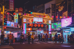taipei - Jaya Travel & Tours Night market entrance at night with bright neon arches, lanterns, and shoppers walking along stalls under colorful lights in a busy street.