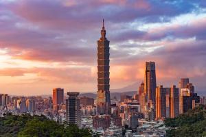 taiwan arrival - Jaya Travel & Tours Sunset cityscape of Taipei with the tall Taipei 101 skyscraper rising above surrounding buildings and a pink-orange sky.