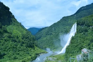 jang-waterfall-tawang - Jaya Travel & Tours Waterfall spills down a lush green canyon into a winding river with mist in a valley landscape