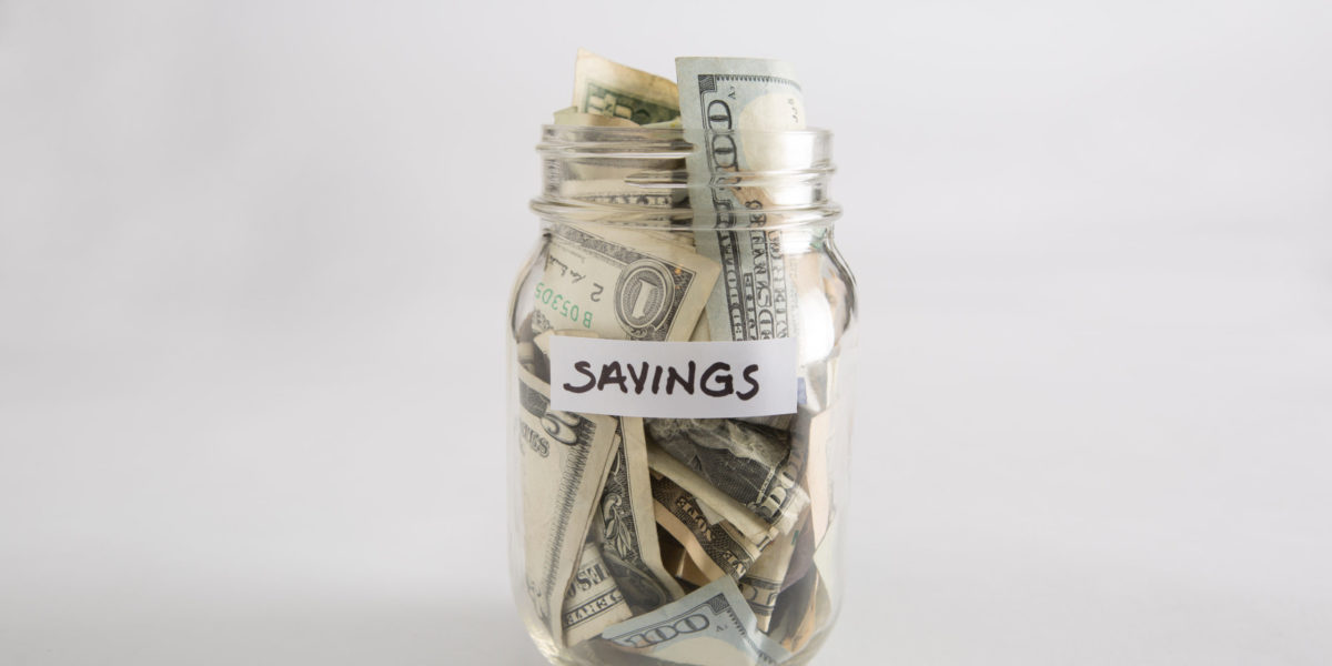 a mason jar full of money labeled savings that someone wants to use to travel and book travel agents.