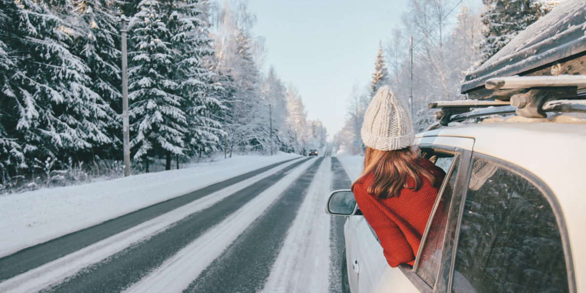 A woman looking out the car window at a scenic winter highway through a forest with snow.