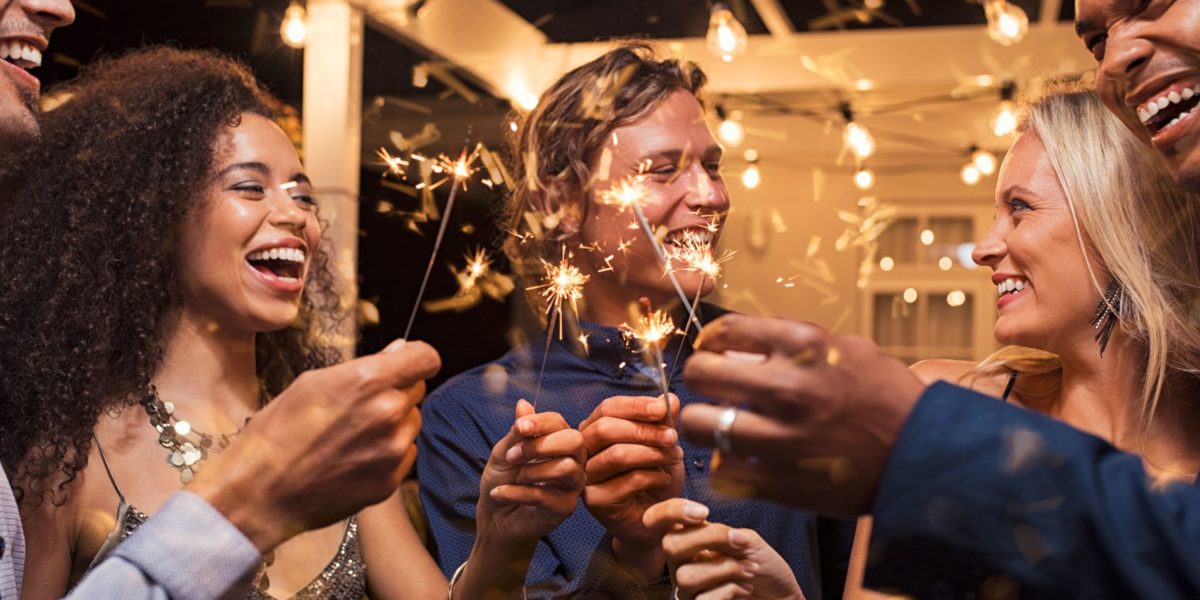 friends celebrate New Year's Eve with sparklers and drinks because they couldn't travel to Brazil or Scotland with Jaya.