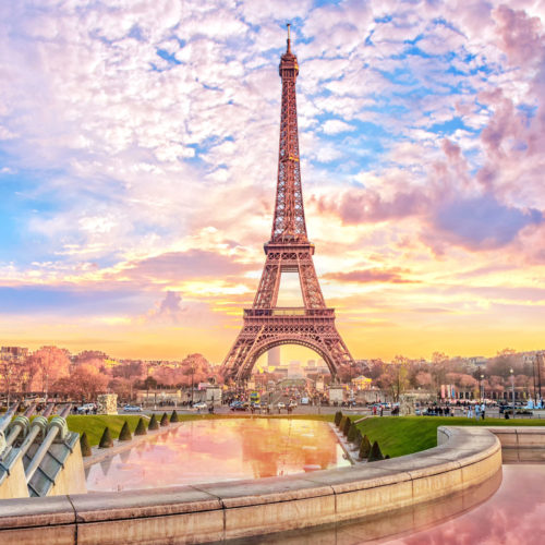 The tourist spot Eiffel Tower stands tall in front of a sunset in Paris, France against a romantic travel tours vacation background.