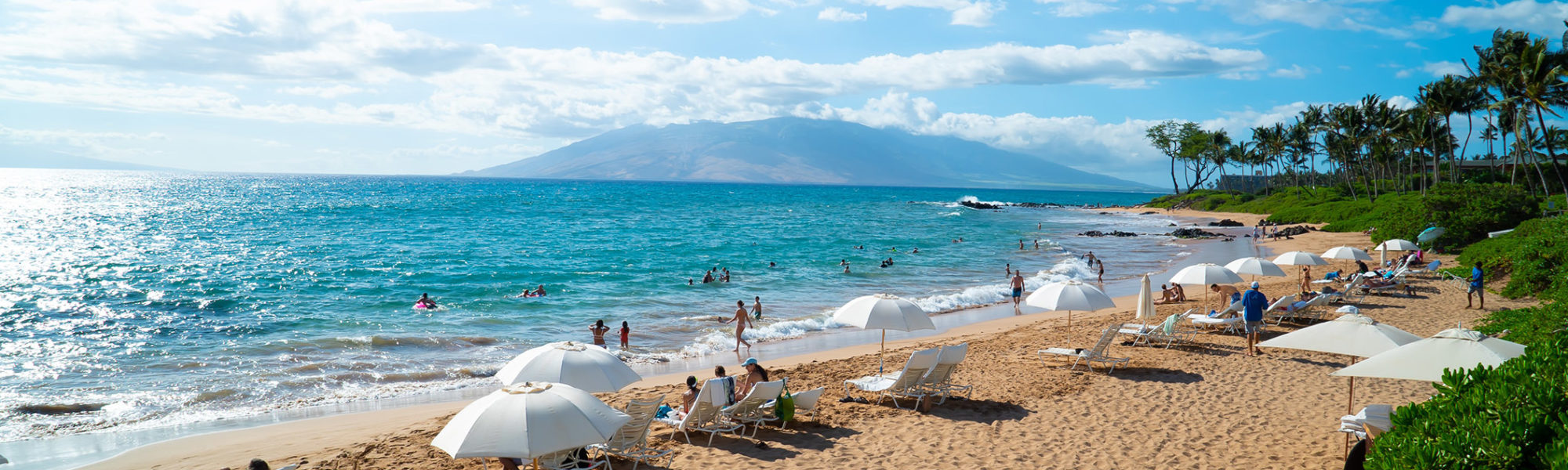 Travelers relaxing at the sandy beach with the blue ocean on the Island of Maui, Hawaii USA in a vacation crafted by Jaya Travel & Tours.