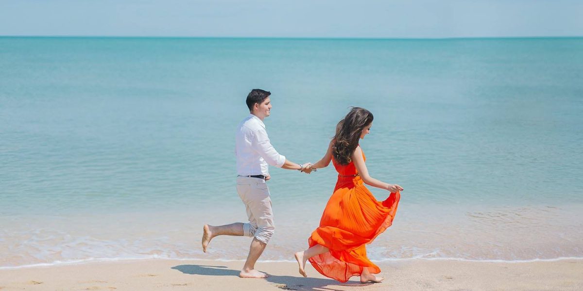 A young married couple hand in hand joyfully running on a sandy beach for a Valentine's Day Honeymoon destination with Jaya Travel & Tours.