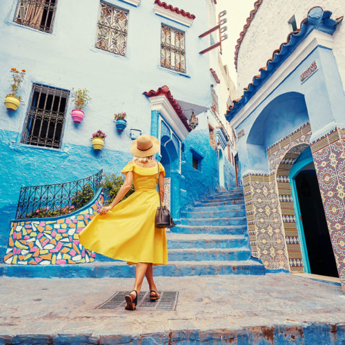 A young woman traveler in a yellow dress walks in the medina of the blue city Chefchaouen in Morocco after purchasing one of Jaya Travel & Tours travel promotions.